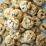 Chocolate chip cookies stacked together on a piece of parchment paper.