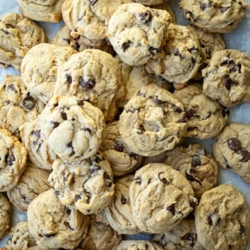 Chocolate chip cookies stacked together on a piece of parchment paper.