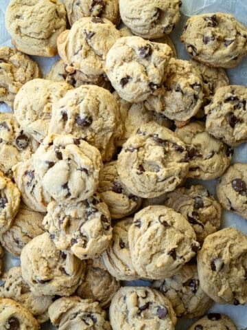 Chocolate chip cookies stacked together on a piece of parchment paper.