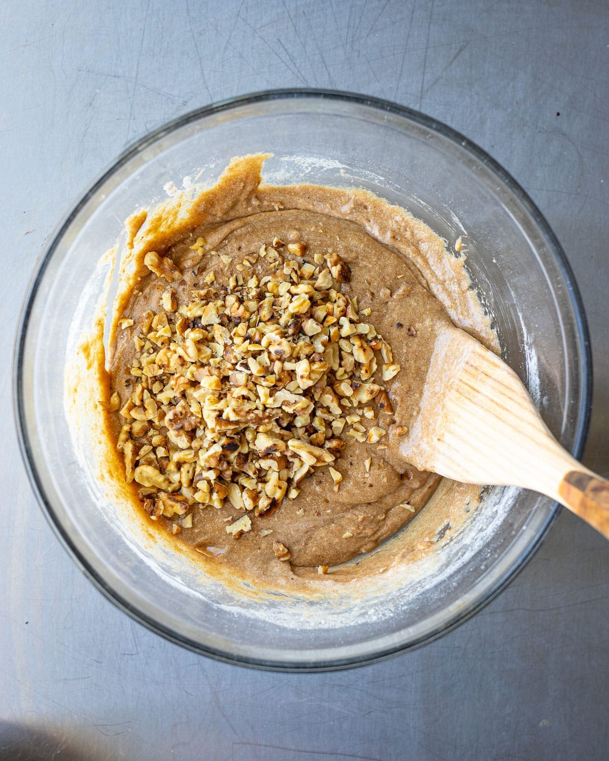Chopped walnuts on muffin batter in a glass bowl with a wooden spoon. 
