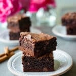 Cinnamon brownies on small white plates with pink flowers in the background.