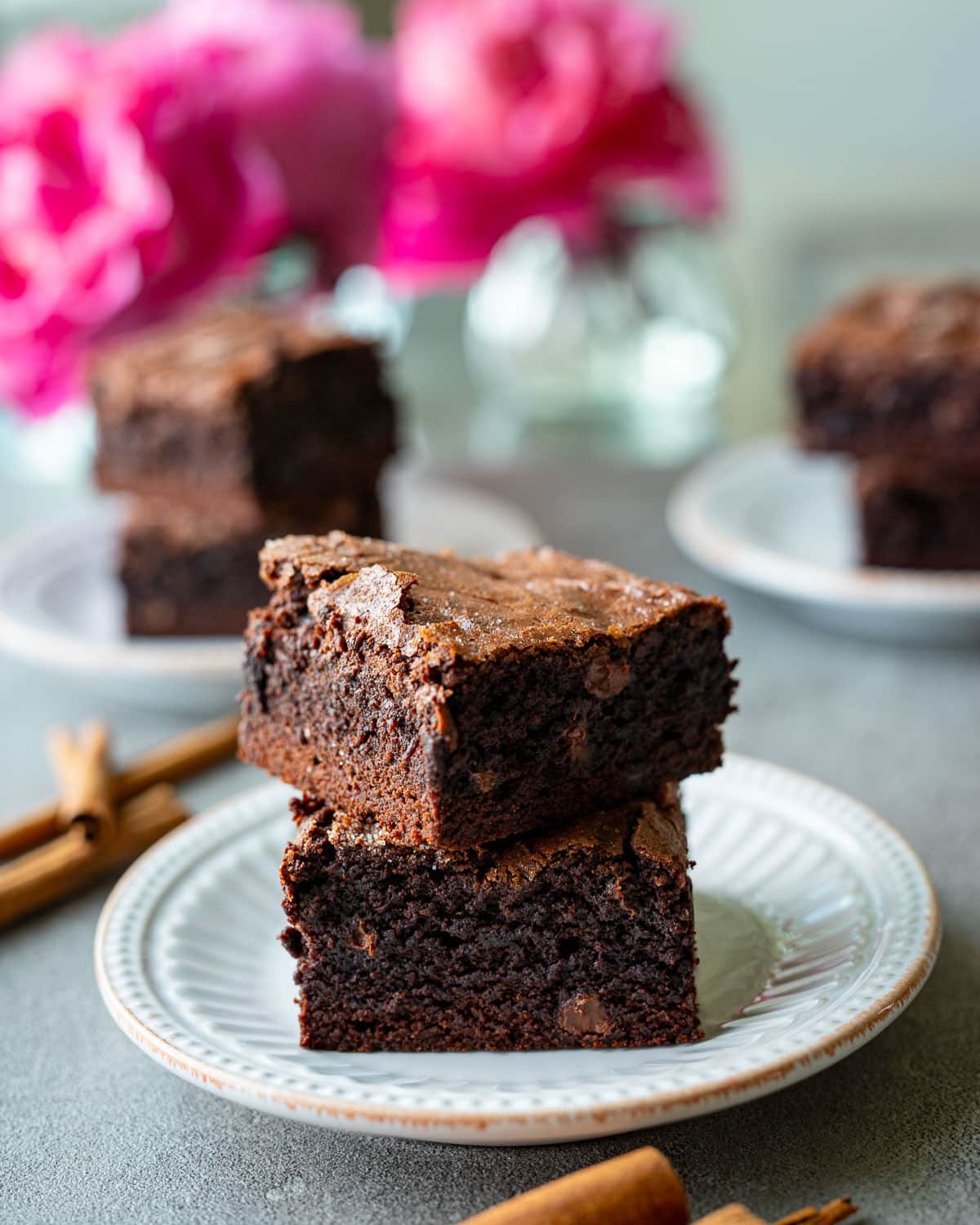 Cinnamon brownies on small white plates with pink flowers in the background.