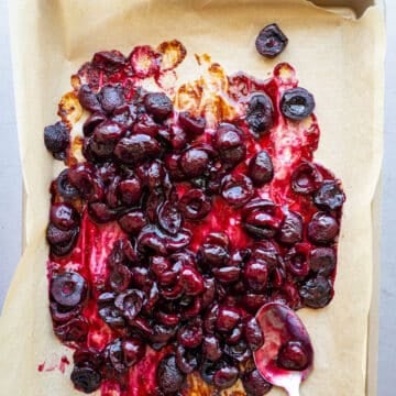 Roasted cherries on a baking sheet lined with parchment paper.