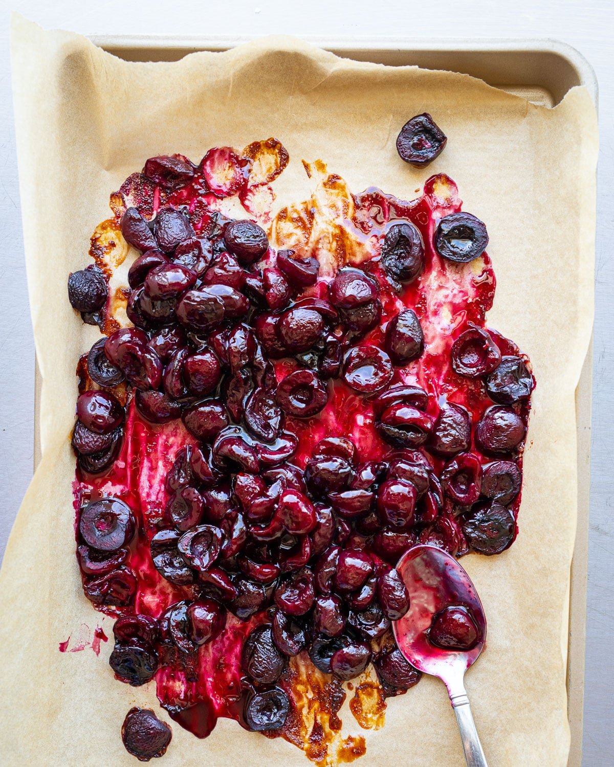 Roasted cherries on a baking sheet lined with parchment paper. 