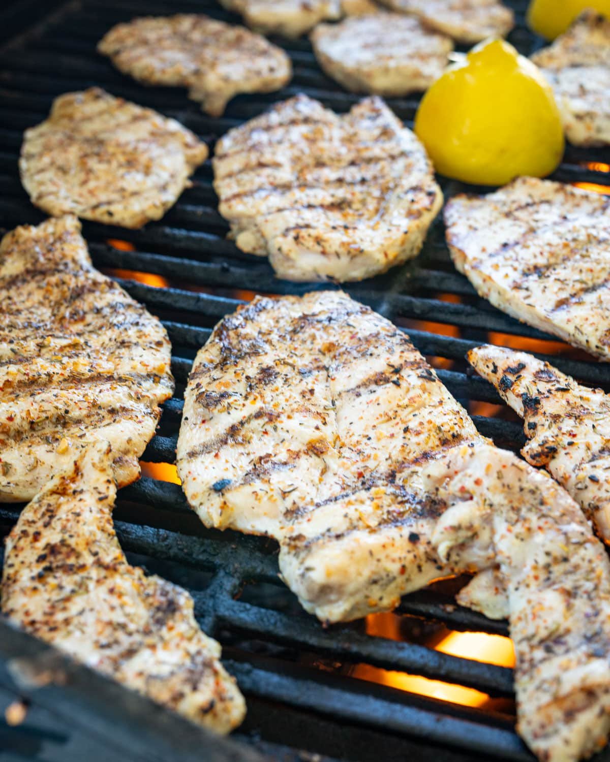 Chicken and a halved lemon grilling on a gas grill. 