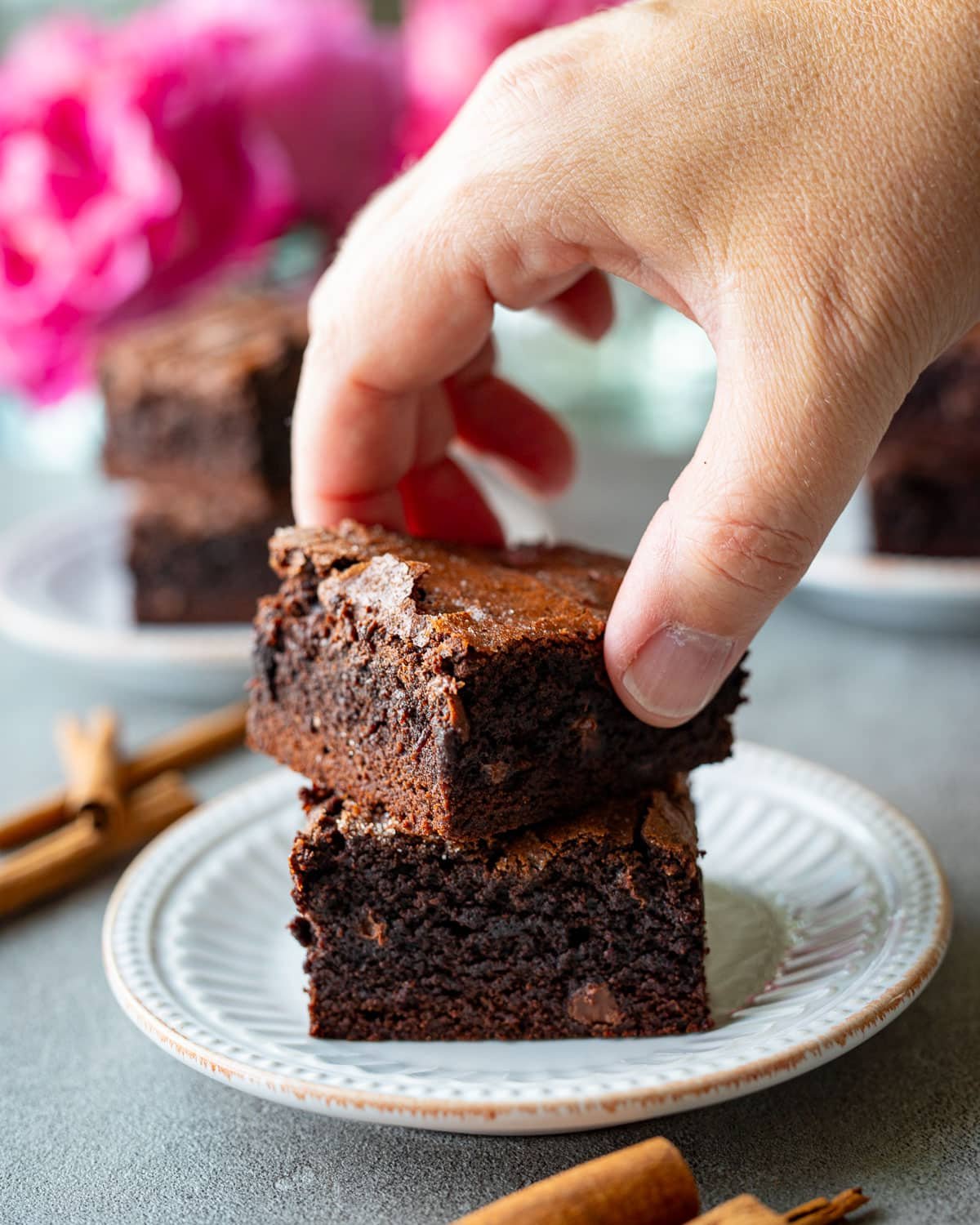 Woman grabbing a cinnamon brownie from a small white plate.