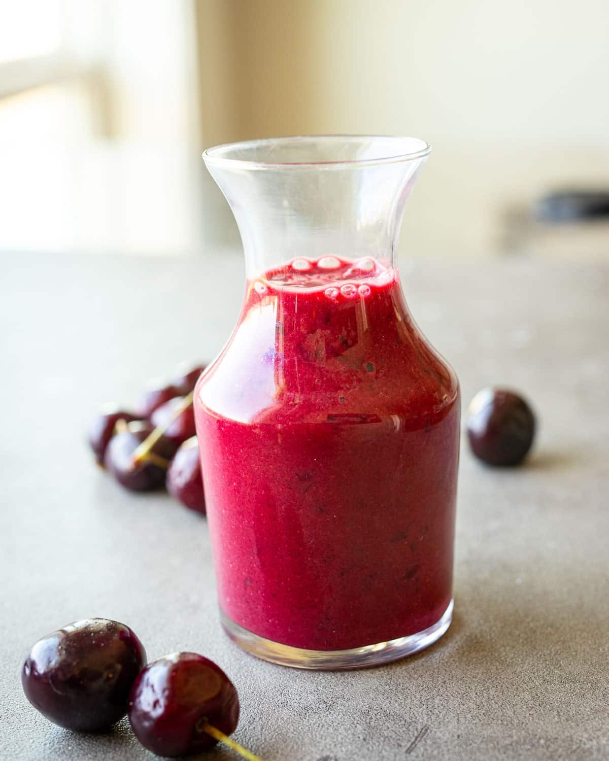 Cherry vinaigrette in a small glass jar on a counter with fresh cherries on the side. 