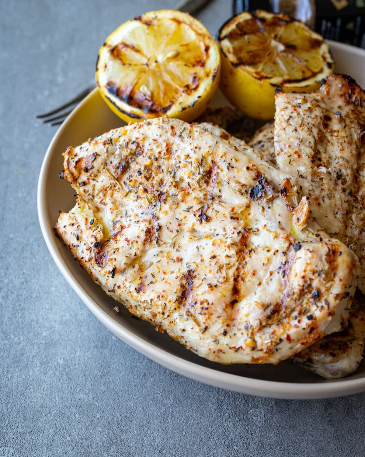 Italian grilled chicken stacked in a ceramic bowl with grilled lemons in it. 