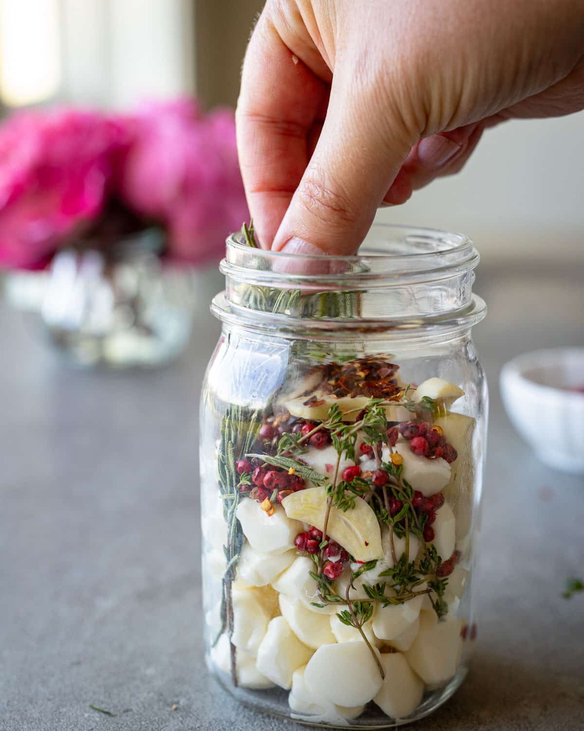 Woman adding herbs to fresh mozzarella in a mason jar.