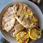 Grilled Italian herb chicken cutlets in a ceramic bowl with a grilled lemon on the side.
