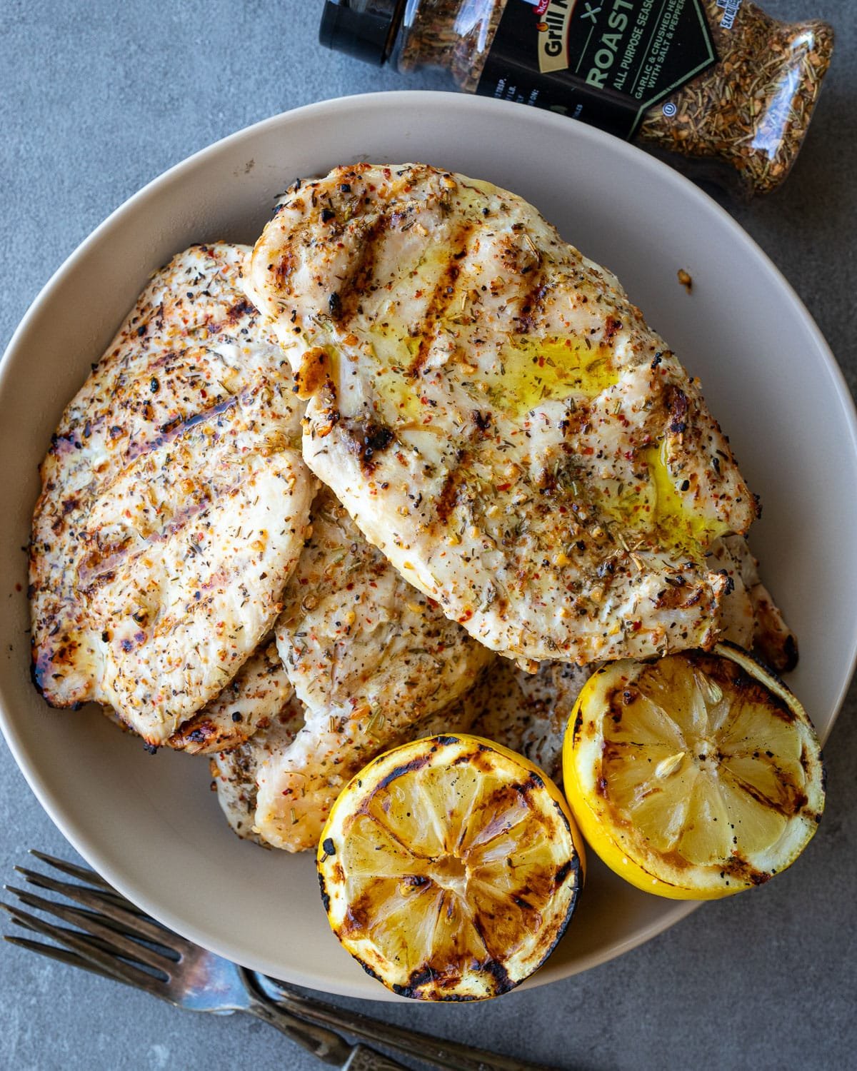 Grilled Italian herb chicken cutlets in a ceramic bowl with a grilled lemon on the side. 