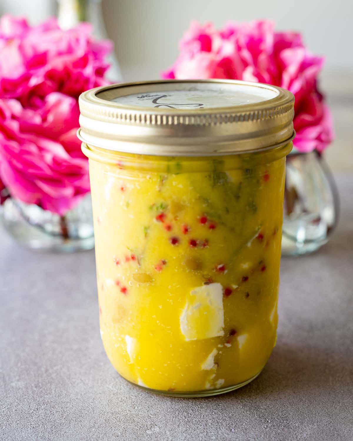 Marinated Greek feta recipe in a mason jar with pink flowers in the background. 