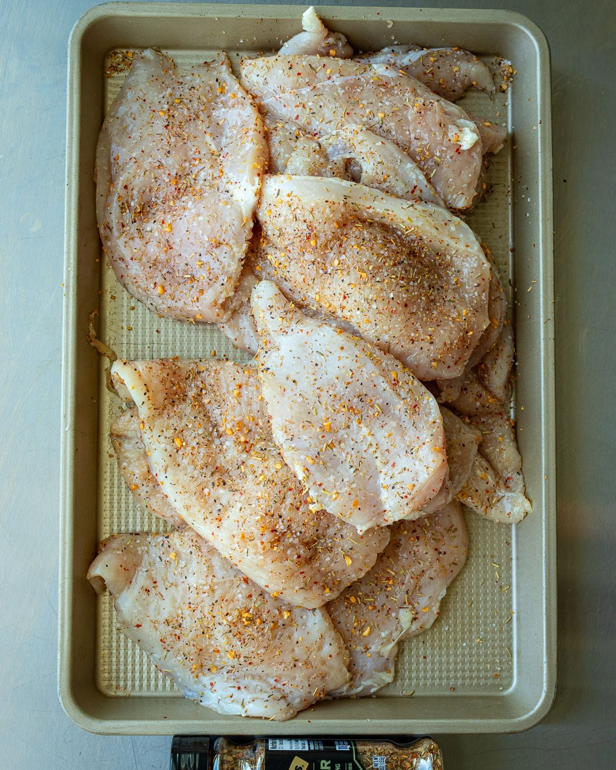 Chicken covered in herb seasoning ready to be grilled on a metal tray. 