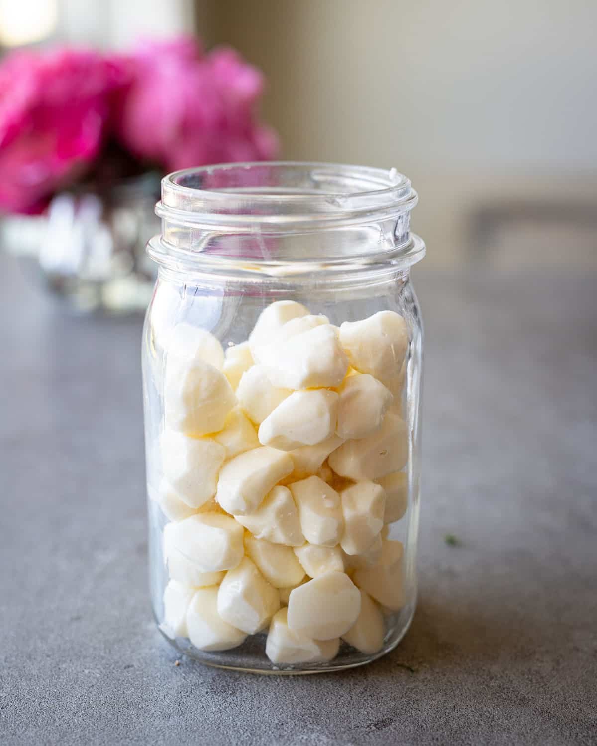 Fresh mozzarella pearls in a mason jar with flowers in the background.