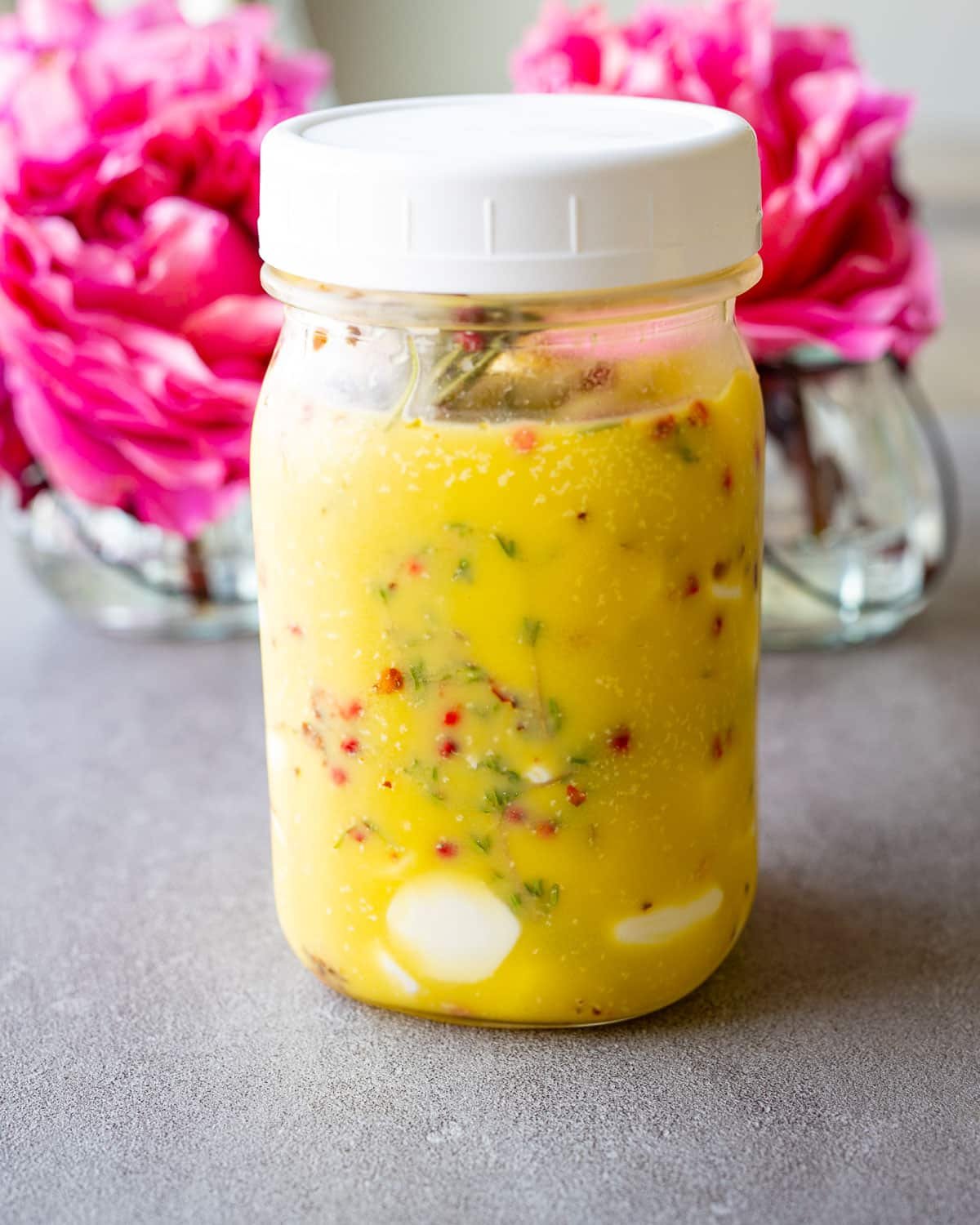 Marinated mozzarella in a mason jar with pink flowers in the background.