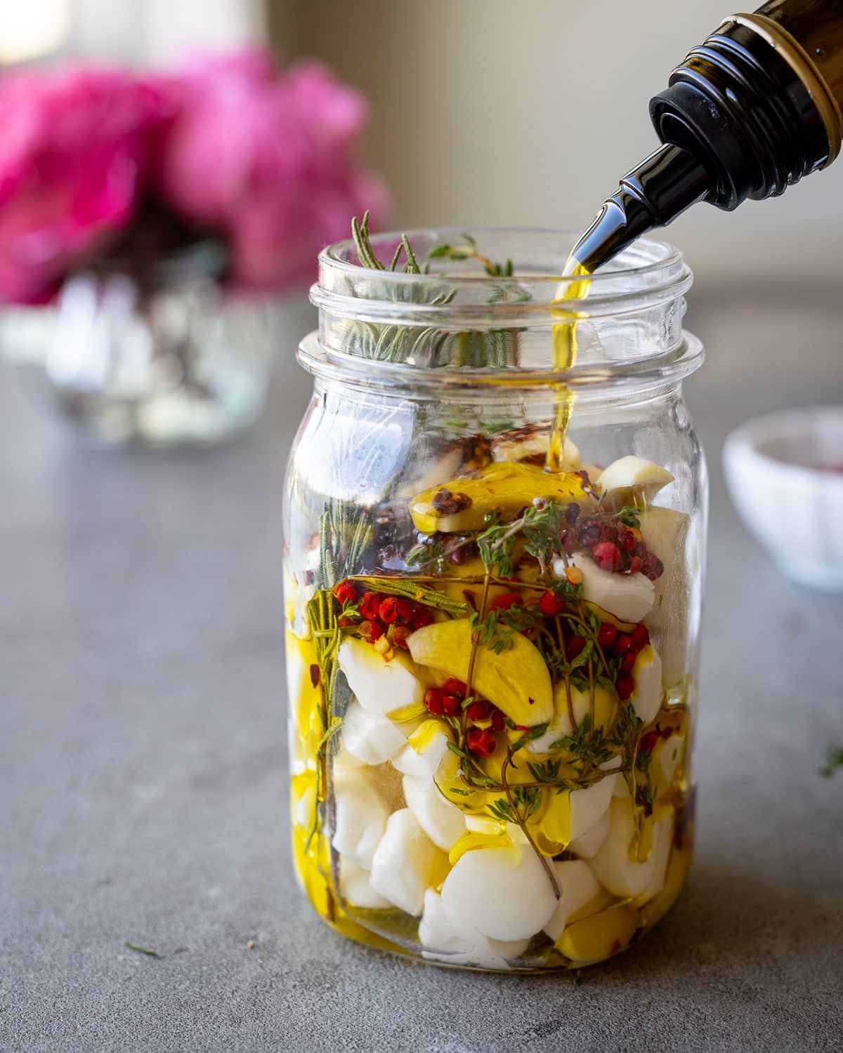 Woman pouring olive oil into a jar with mozzarella and herbs and garlic.