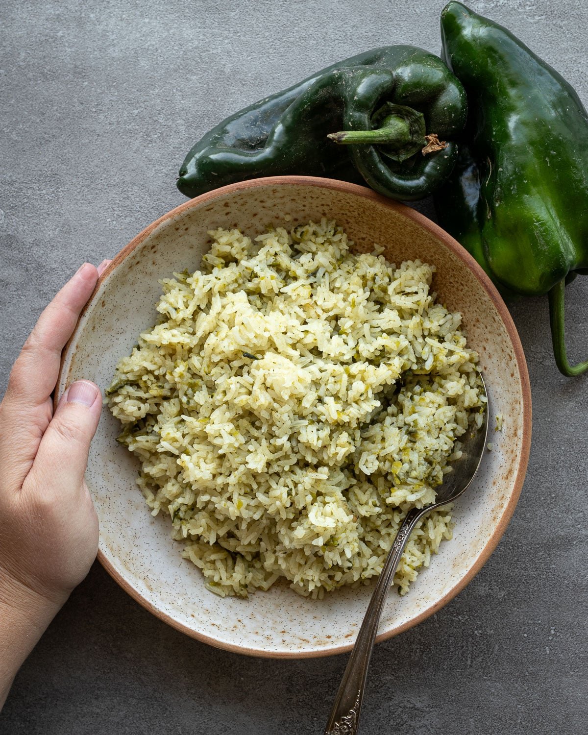 Woman holding a bowl of poblano rice in a ceramic bowl with fresh poblanos on the side. 