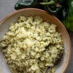 Poblano rice in a ceramic bowl with fresh poblanos on the side.