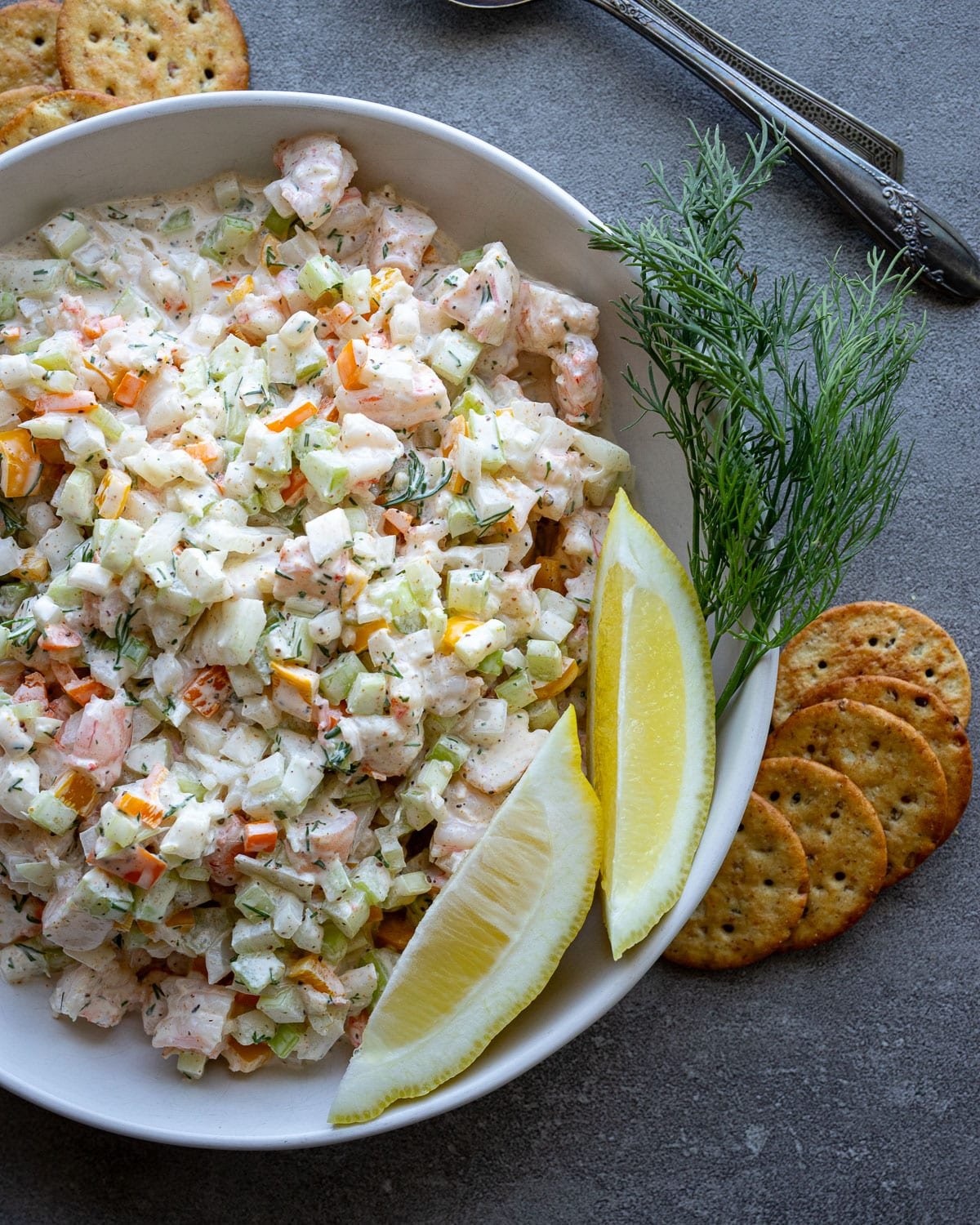 Shrimp salad in a white bowl with lemon wedges on the side and fresh dill.