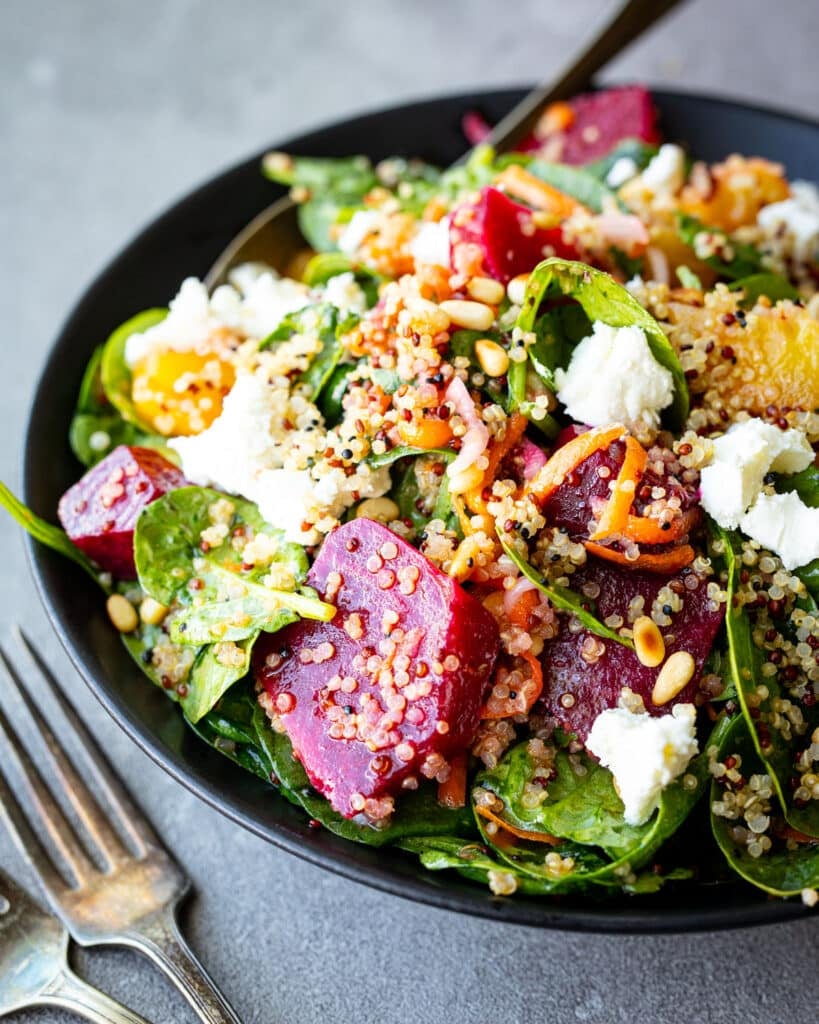 Roasted beet and quinoa salad in a black bowl with vintage forks on the side. 
