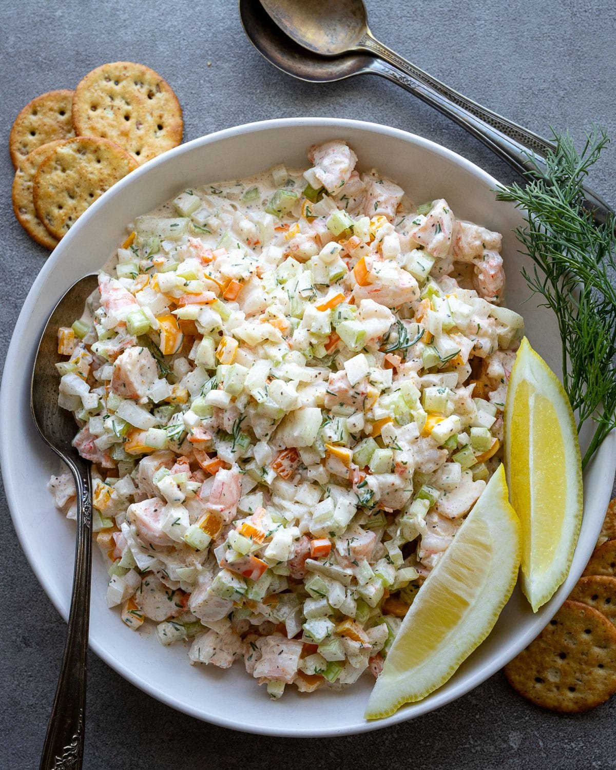 Shrimp salad in a white serving bowl with lemons on the side and fresh dill.