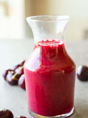 Cherry vinaigrette in a small glass container with fresh cherries on the side.
