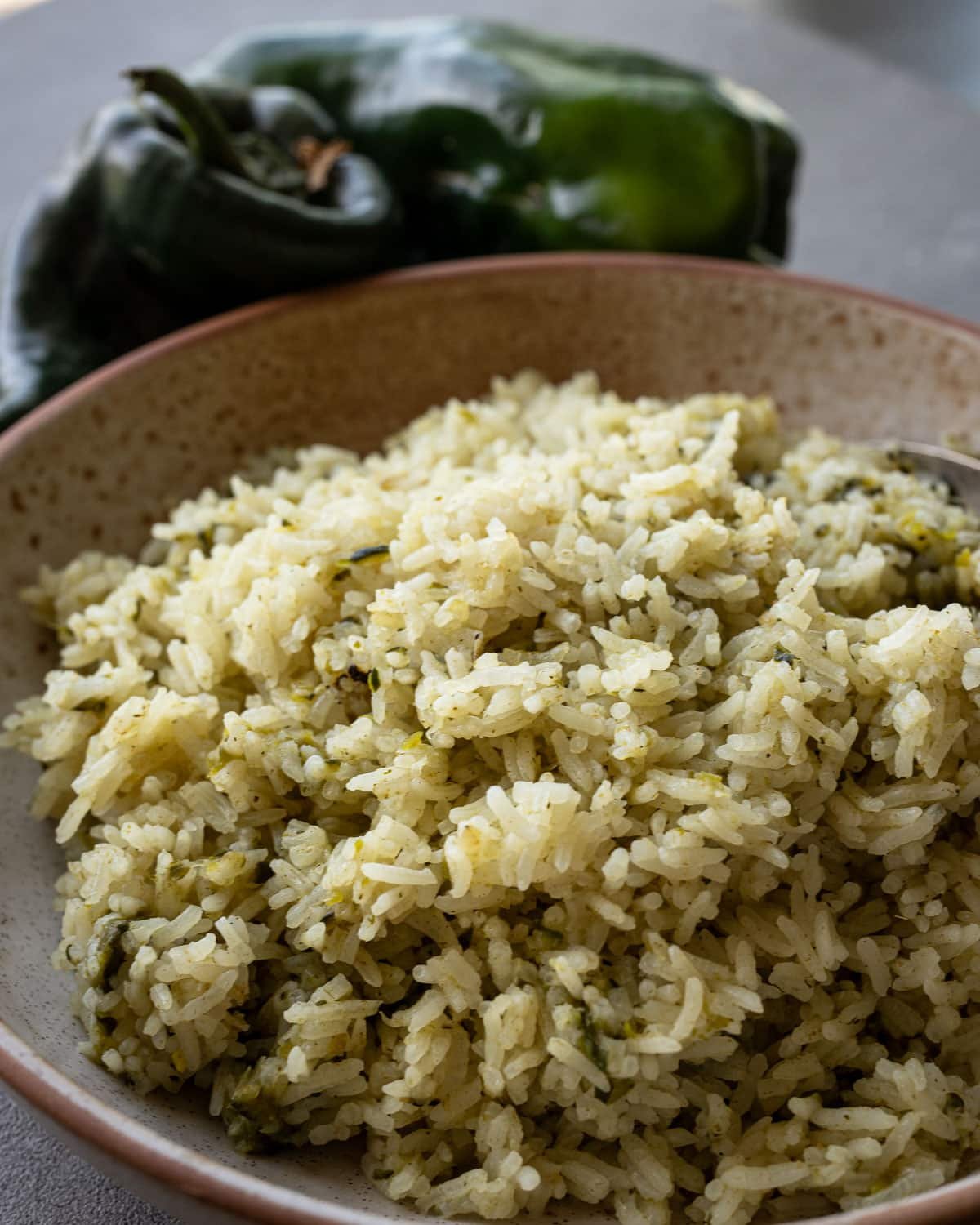 Poblano rice in a ceramic bowl with fresh poblanos on the side. 