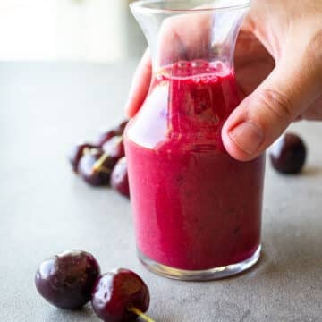 Woman holding a glass container of cherry vinaigrette.