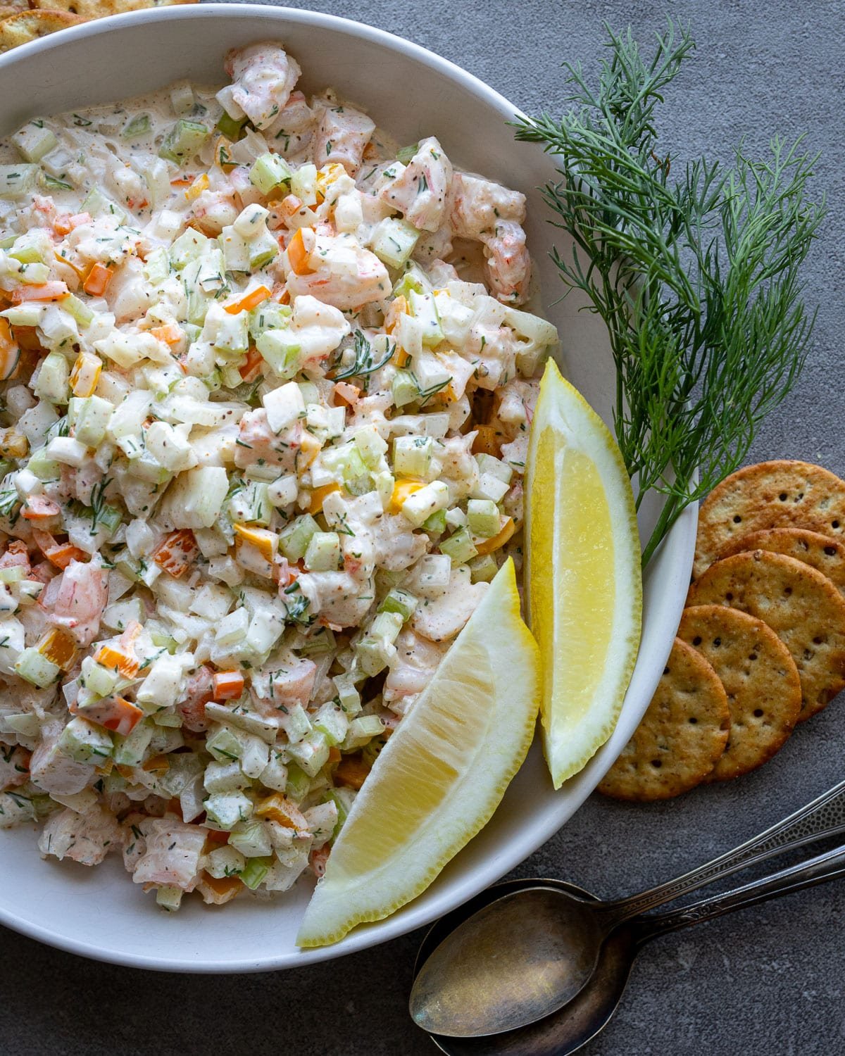 Shrimp salad in a white bowl with crackers on the side and fresh dill.