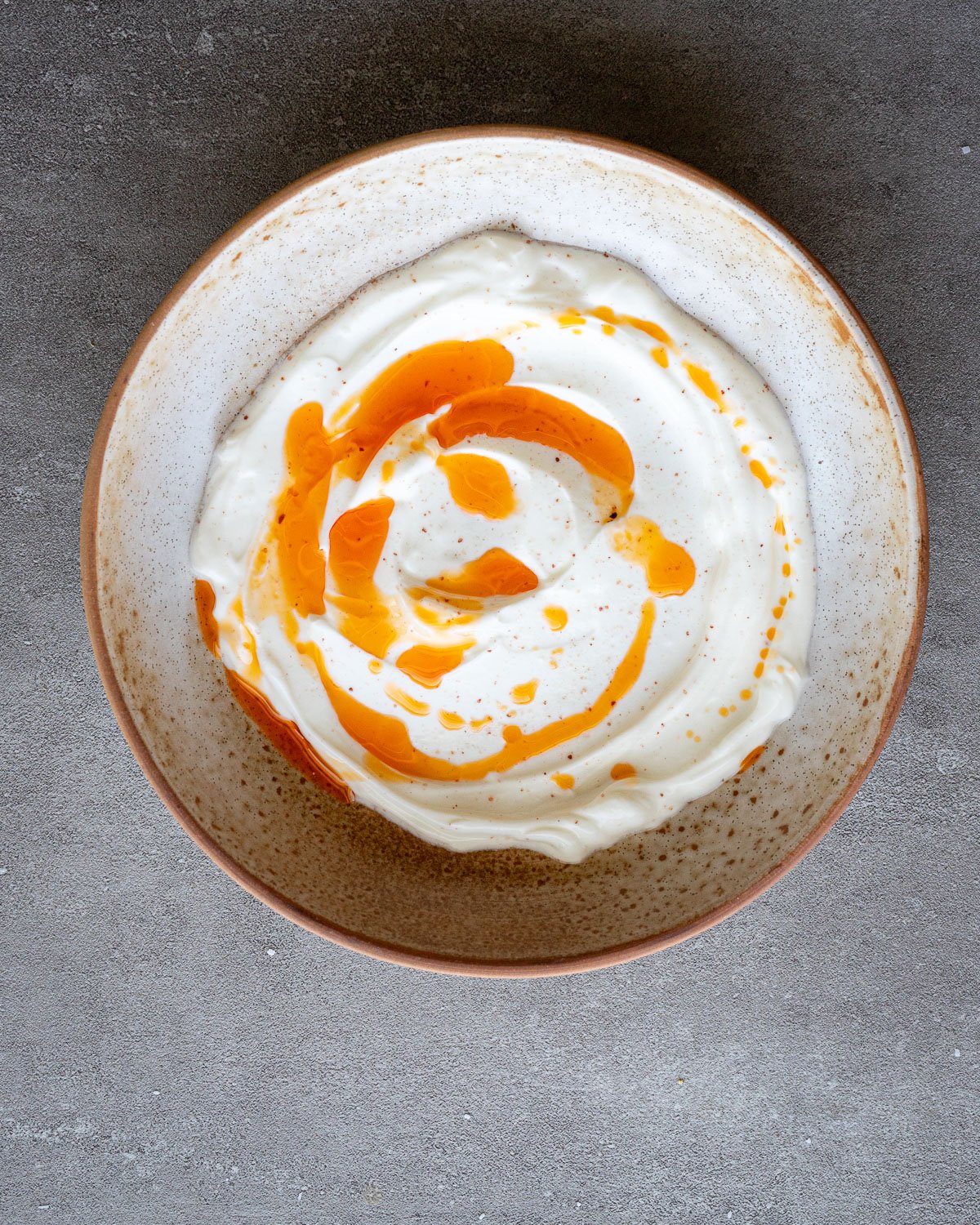 Chili oil drizzled on a spread of Greek yogurt in a ceramic bowl.