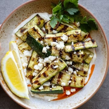 Grilled zucchini in a ceramic bowl with yogurt on the bottom.