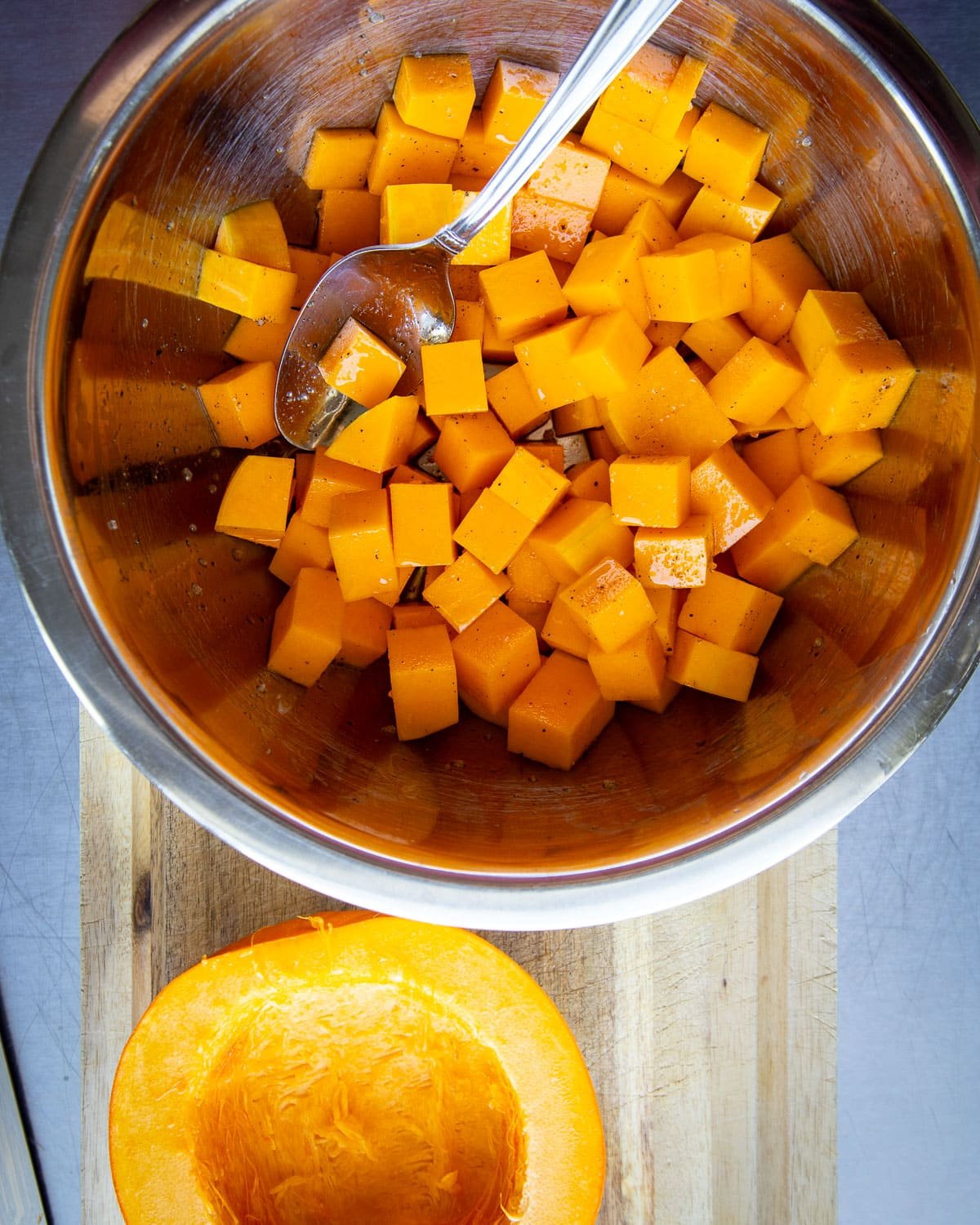 Butternut squash cubed in a metal bowl with a pumpkin on the side.