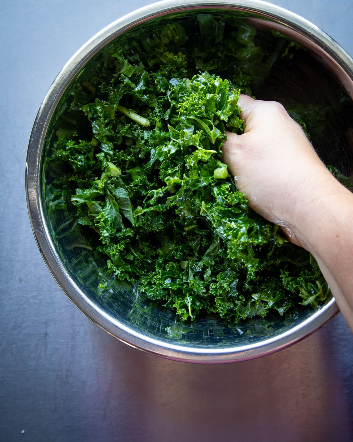 Woman massaging kale in a metal bowl.