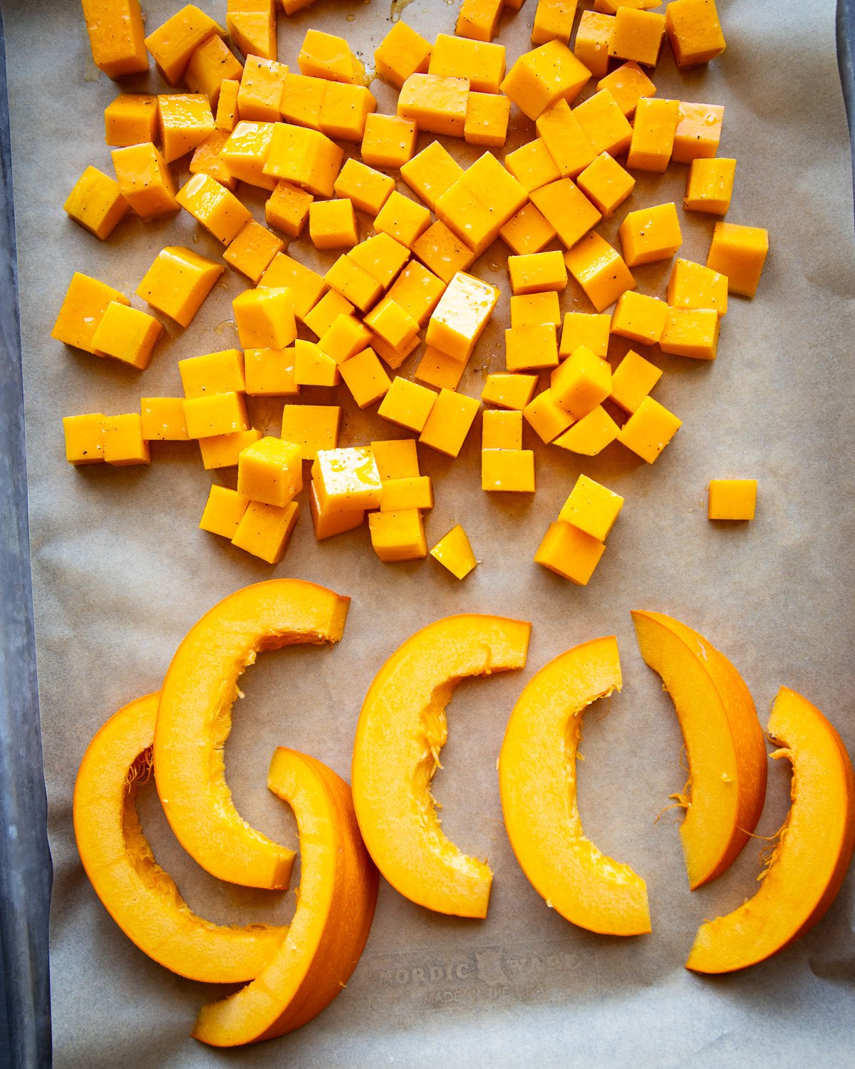 Butternut squash and sliced pumpkin on a parchment lined baking sheet pan.