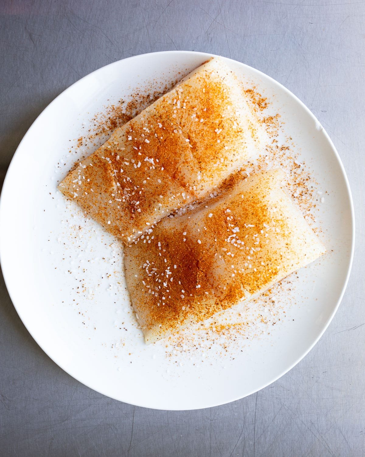 Halibut filet seasoned on a white plate. 