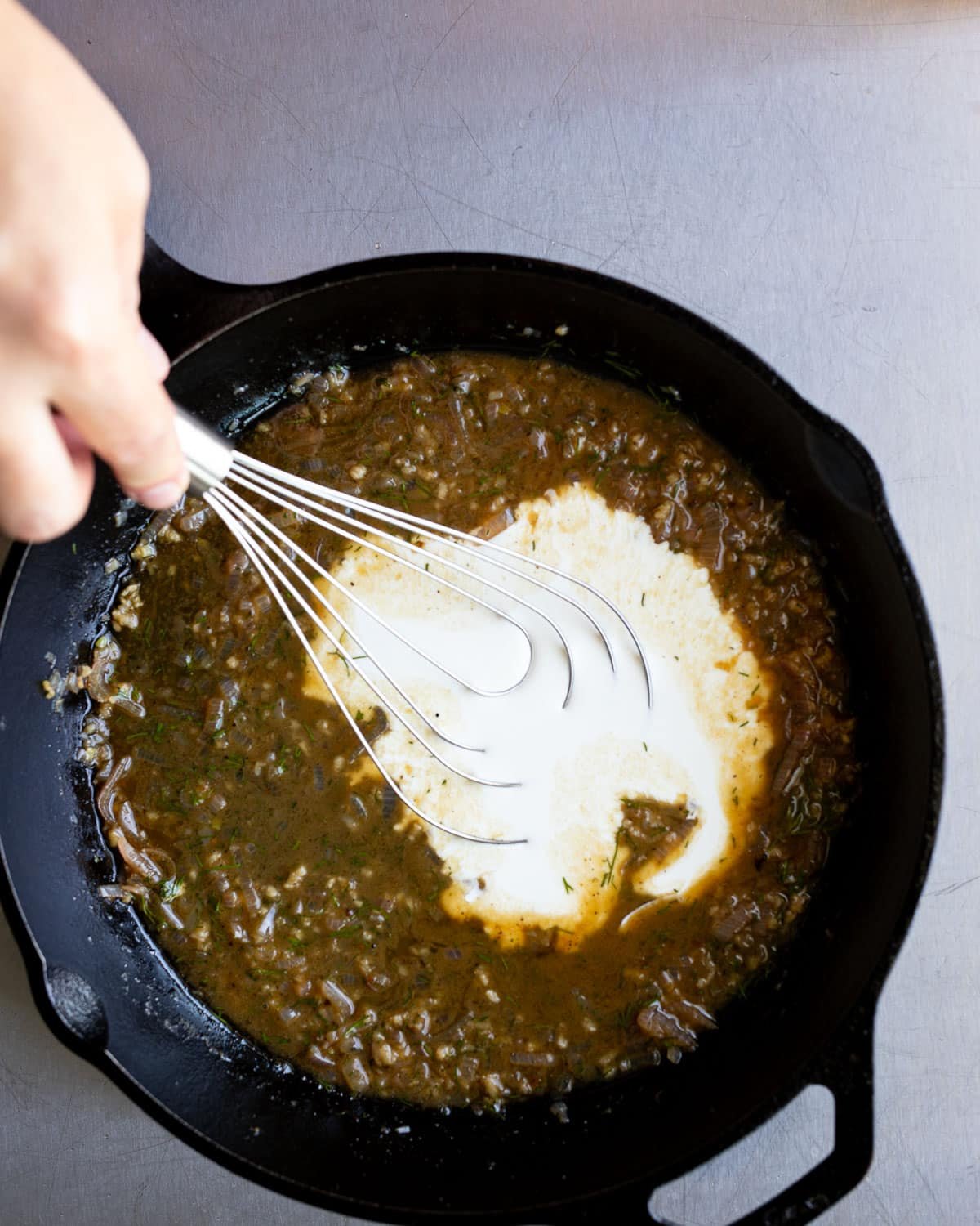 Woman whisking a sauce for halibut in a cast iron pan. 