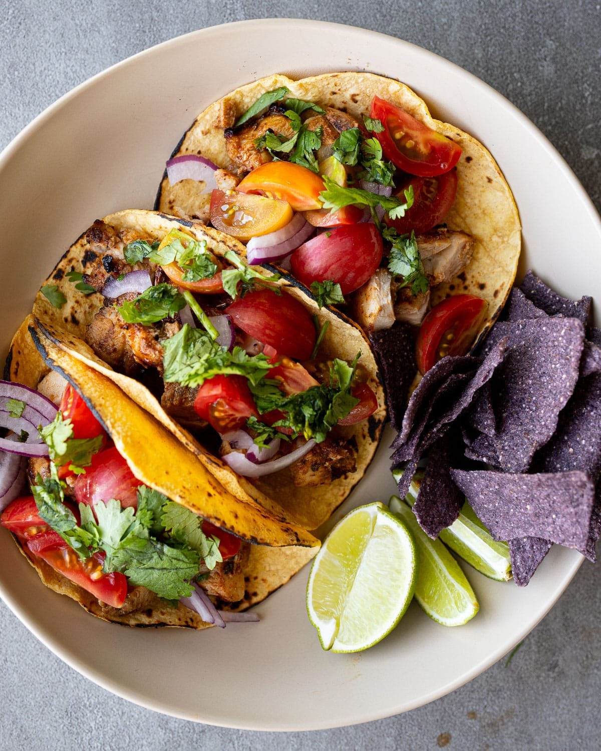 Grilled chicken tacos on a white plate with blue corn chips on the side.