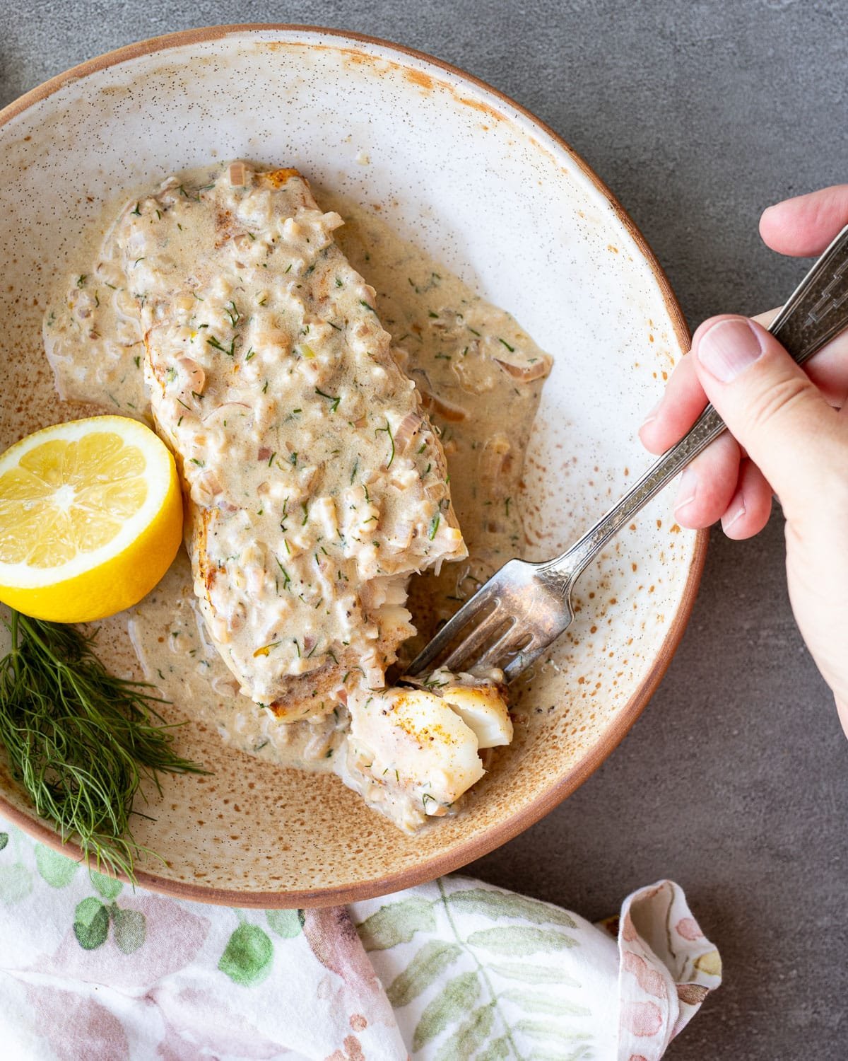 Lemon dill halibut in a ceramic bowl with lemon beside it.