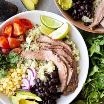 Carne asada bowls in ceramic bowls with avocados, lime, and cilantro on the side.